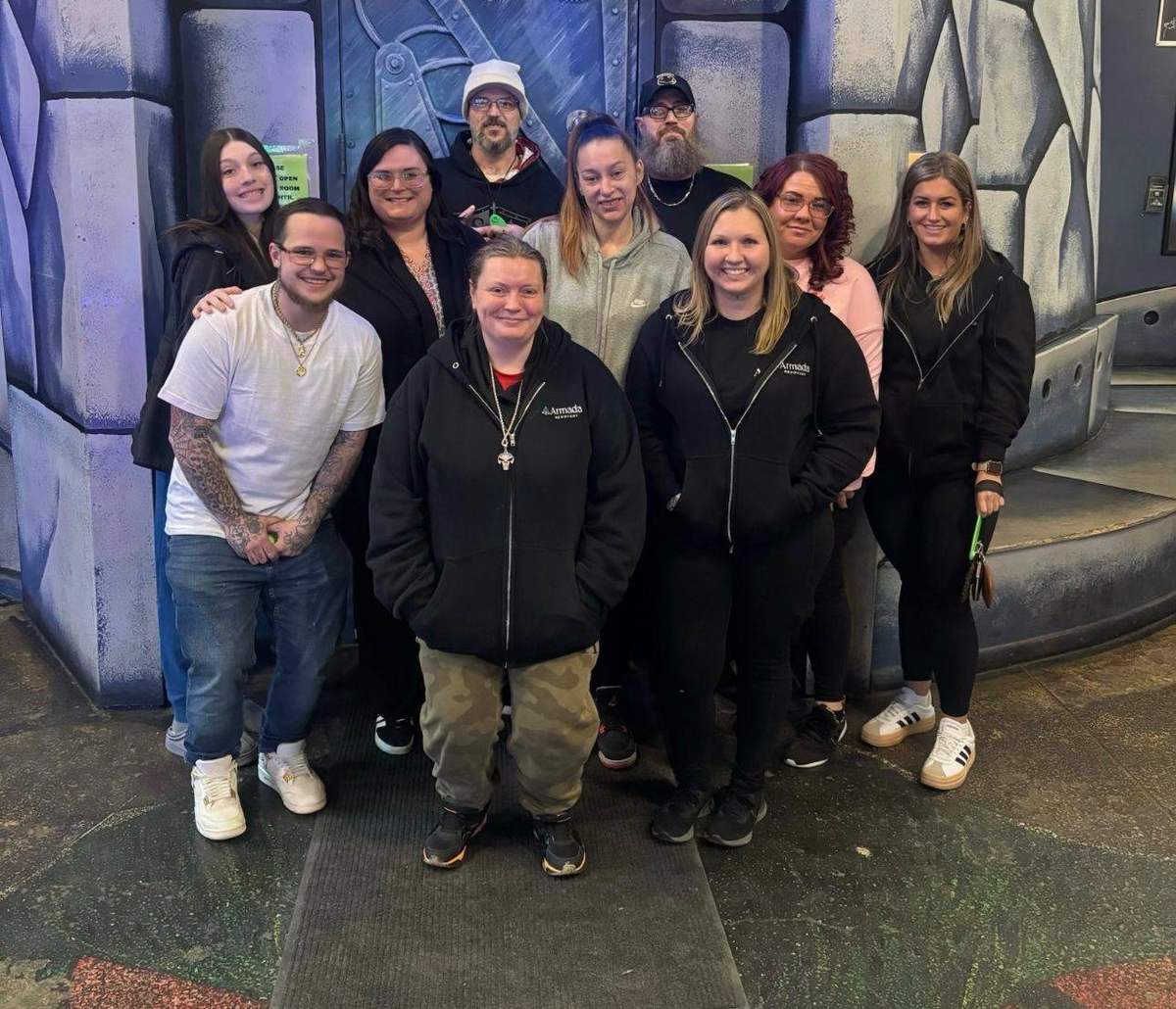 A group of ten smiling in front of an escape room door