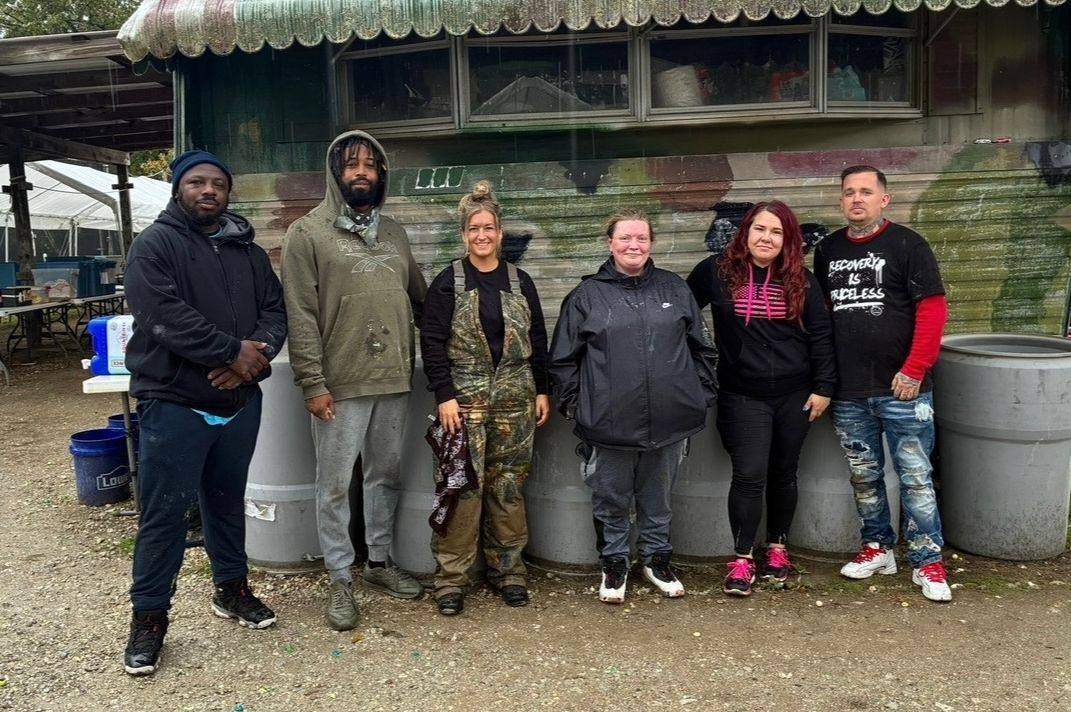 Six people standing together outside a paintball field office