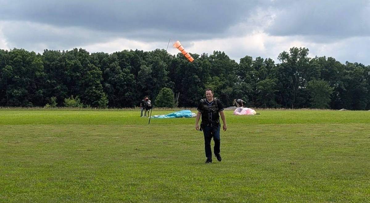A man walking across the landing field after a skydive, parachutes on the grass behind him