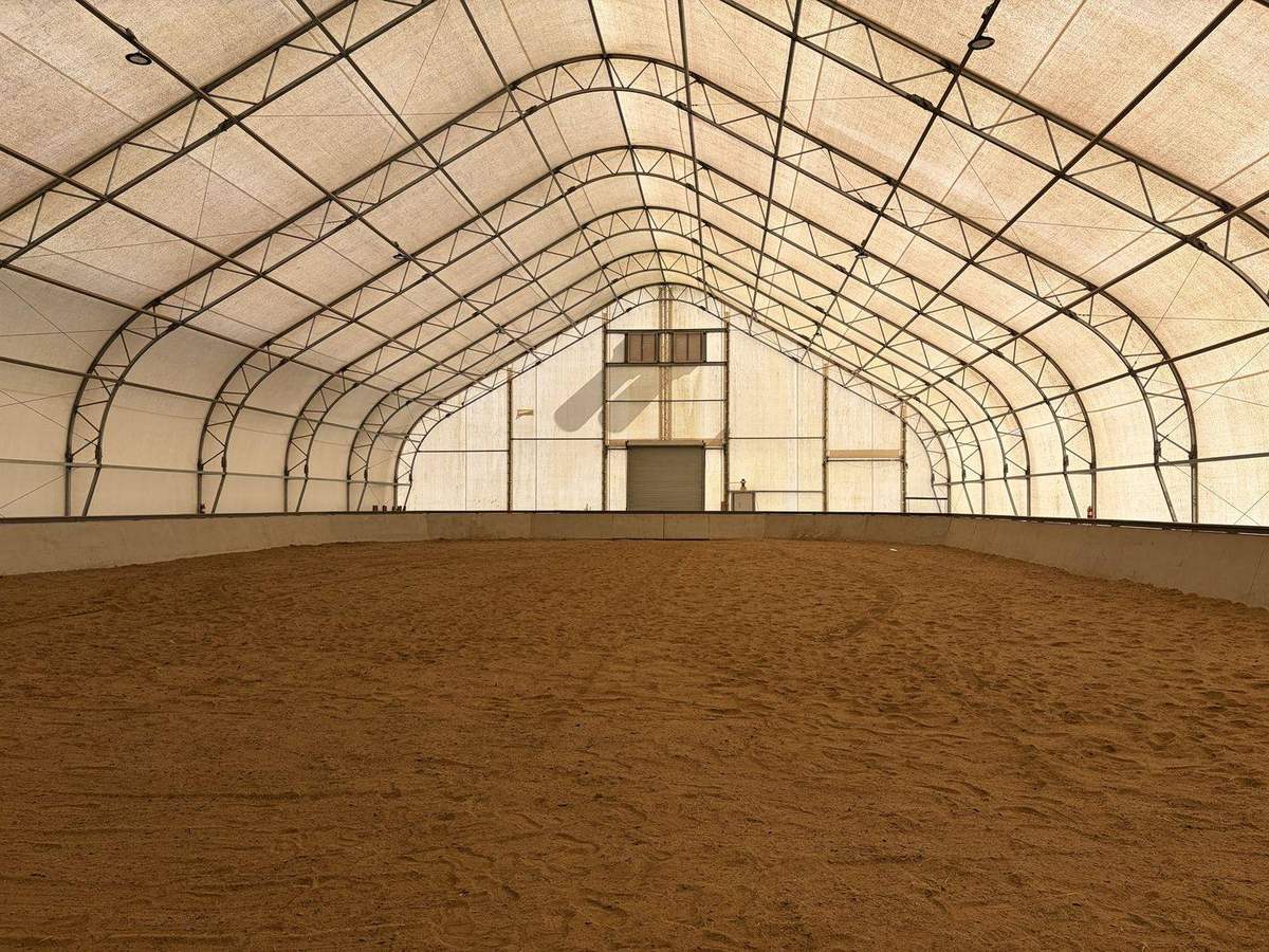 The inside of the covered riding arena, with a dirt floor and an arched roof