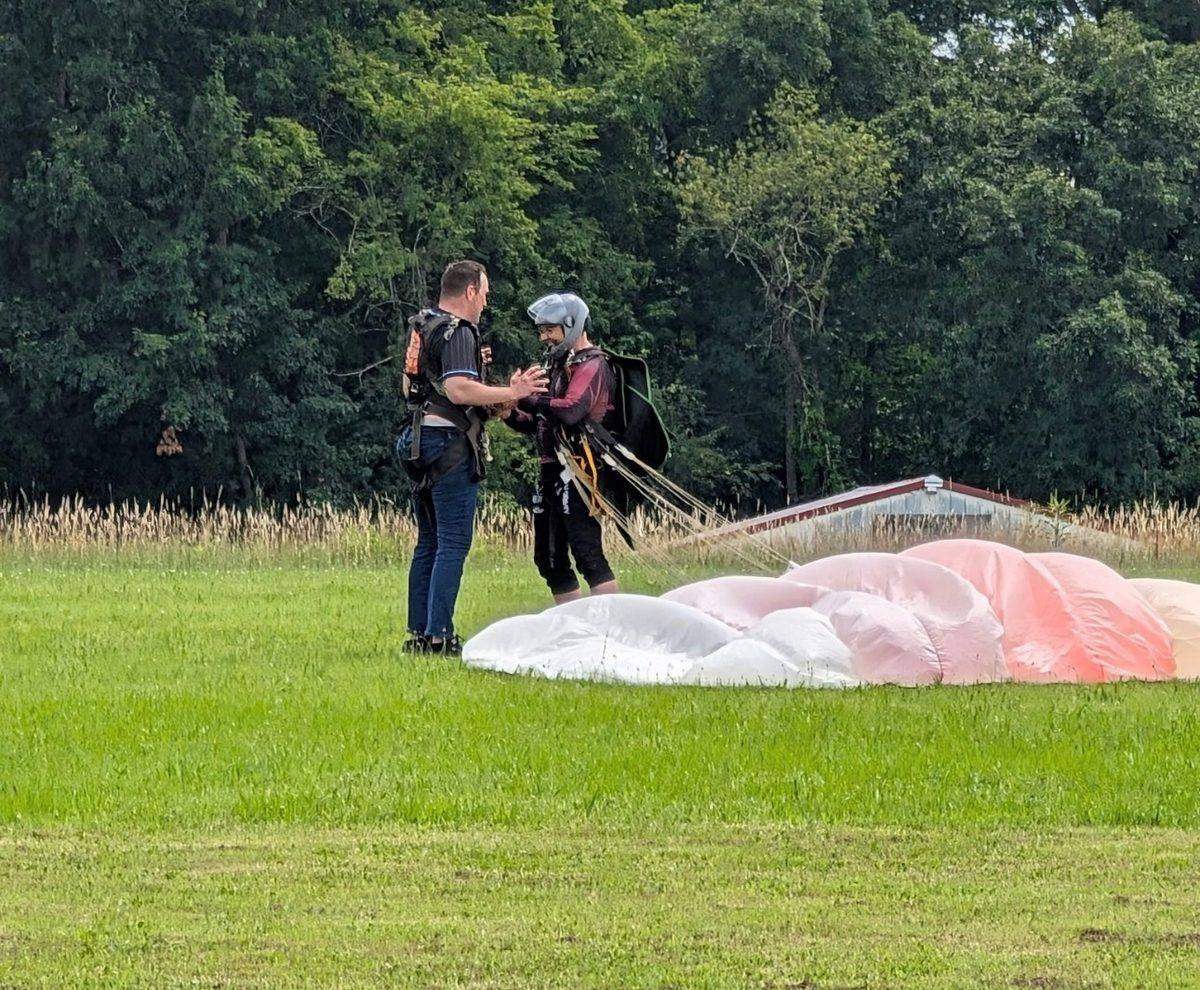 Two people on a grass landing field after a tandem skydive, with the parachute on the ground beside them